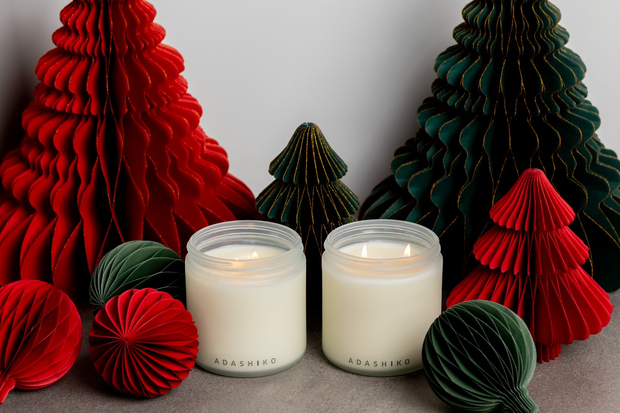 Two Adashiko Christmas Candle jars, wicks lit, next to red and green Christmas decorations | Adashiko Collagen | 100% Natural Skincare