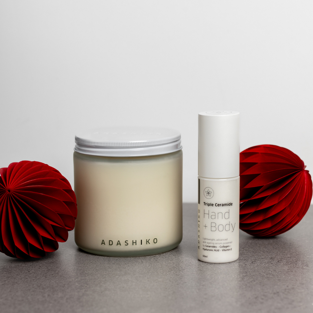 Light + Luxe Due - Adashiko Christmas Candle Jar next to Triple Ceramide Hand + Body bottle on a table with red Christmas baubles | Adashiko Collagen | 100% Natural Skincare 